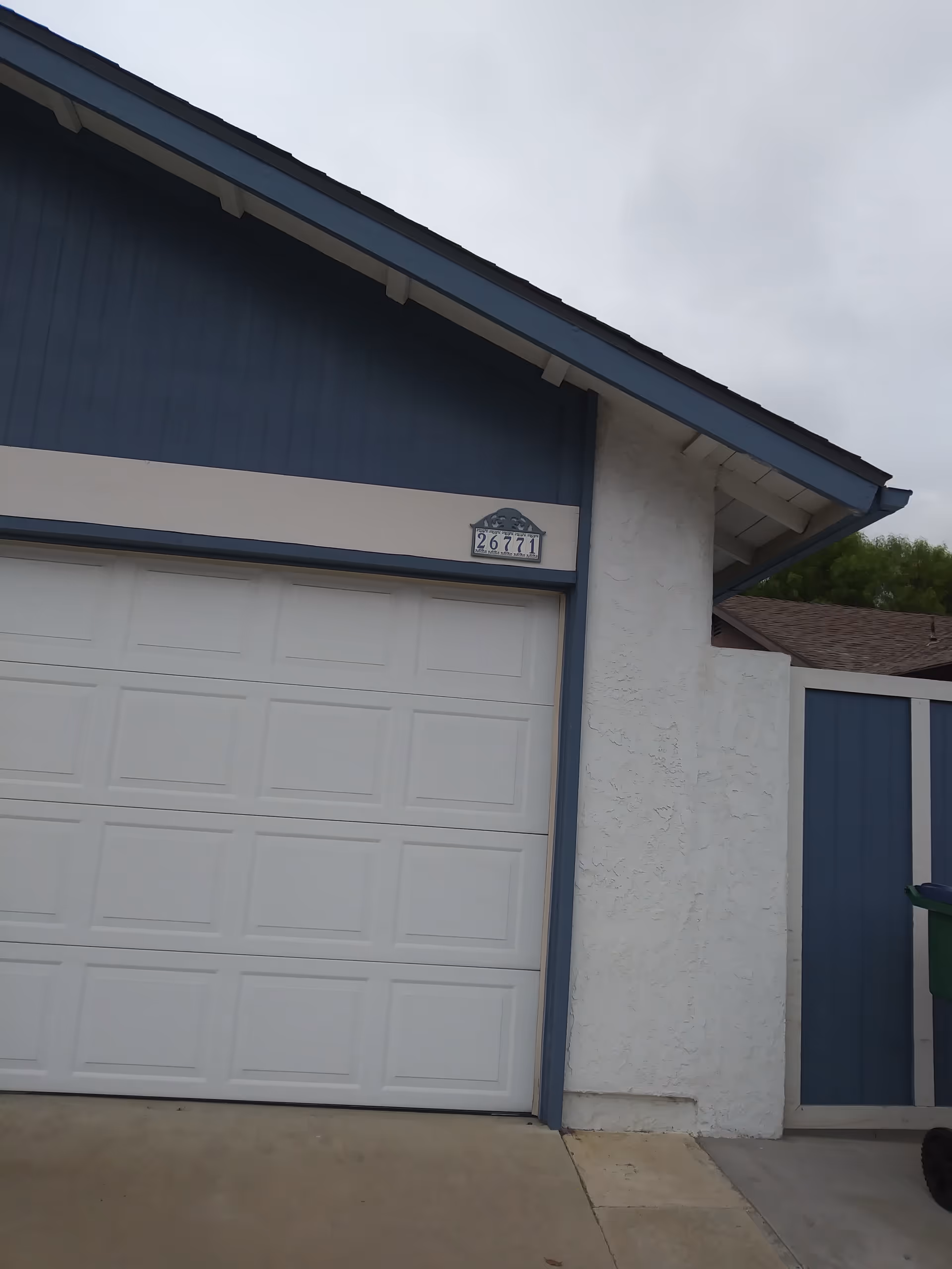 Blue building exterior with a white garage door and a house number plaque.
