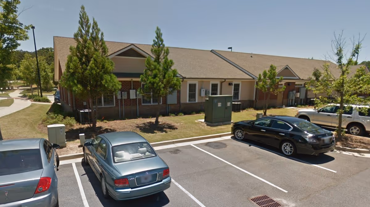 Exterior view of a single-story senior living facility with parked cars and trees.