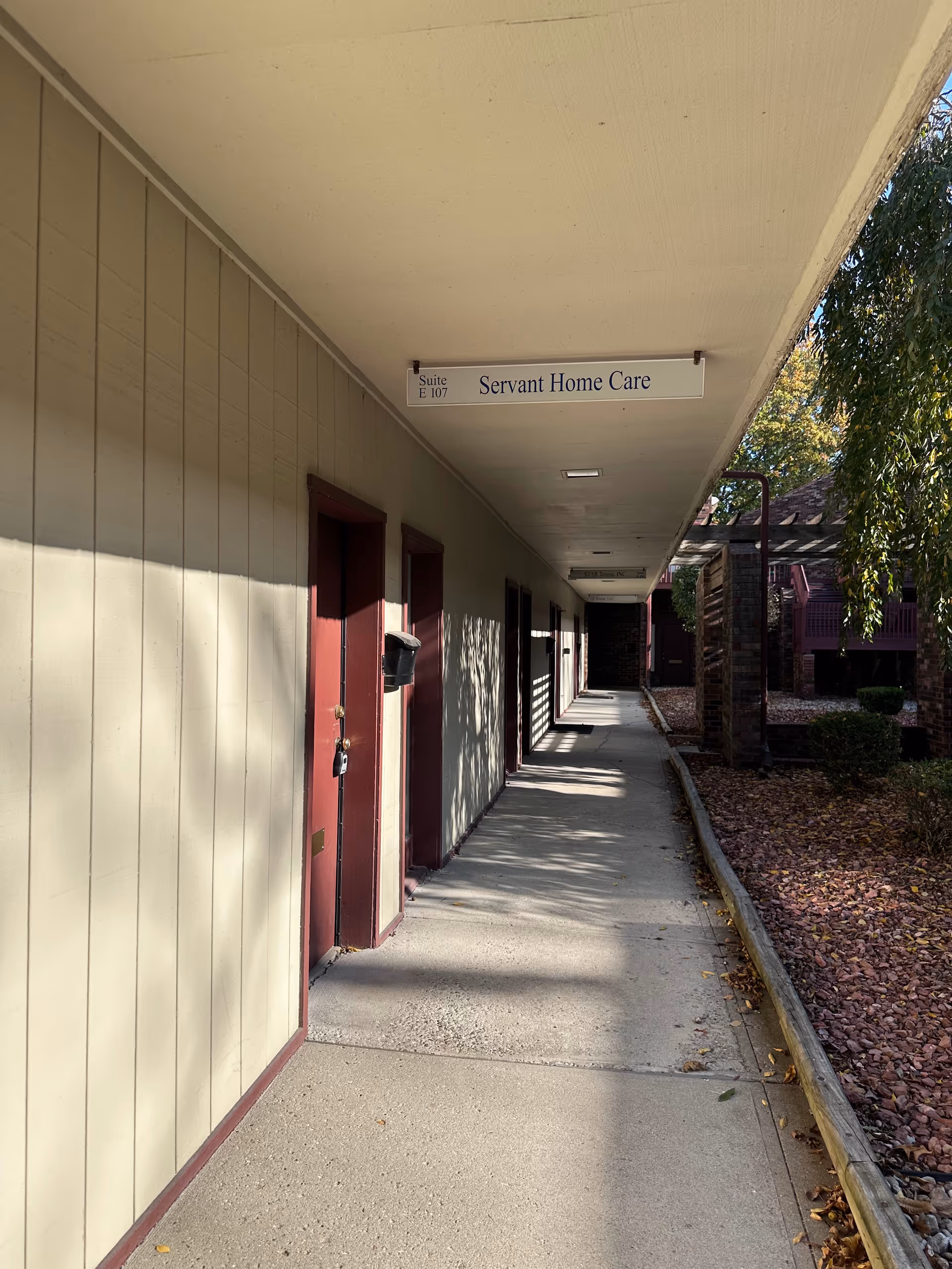 Exterior corridor with beige walls, red doors, and a sign reading Servant Home Care