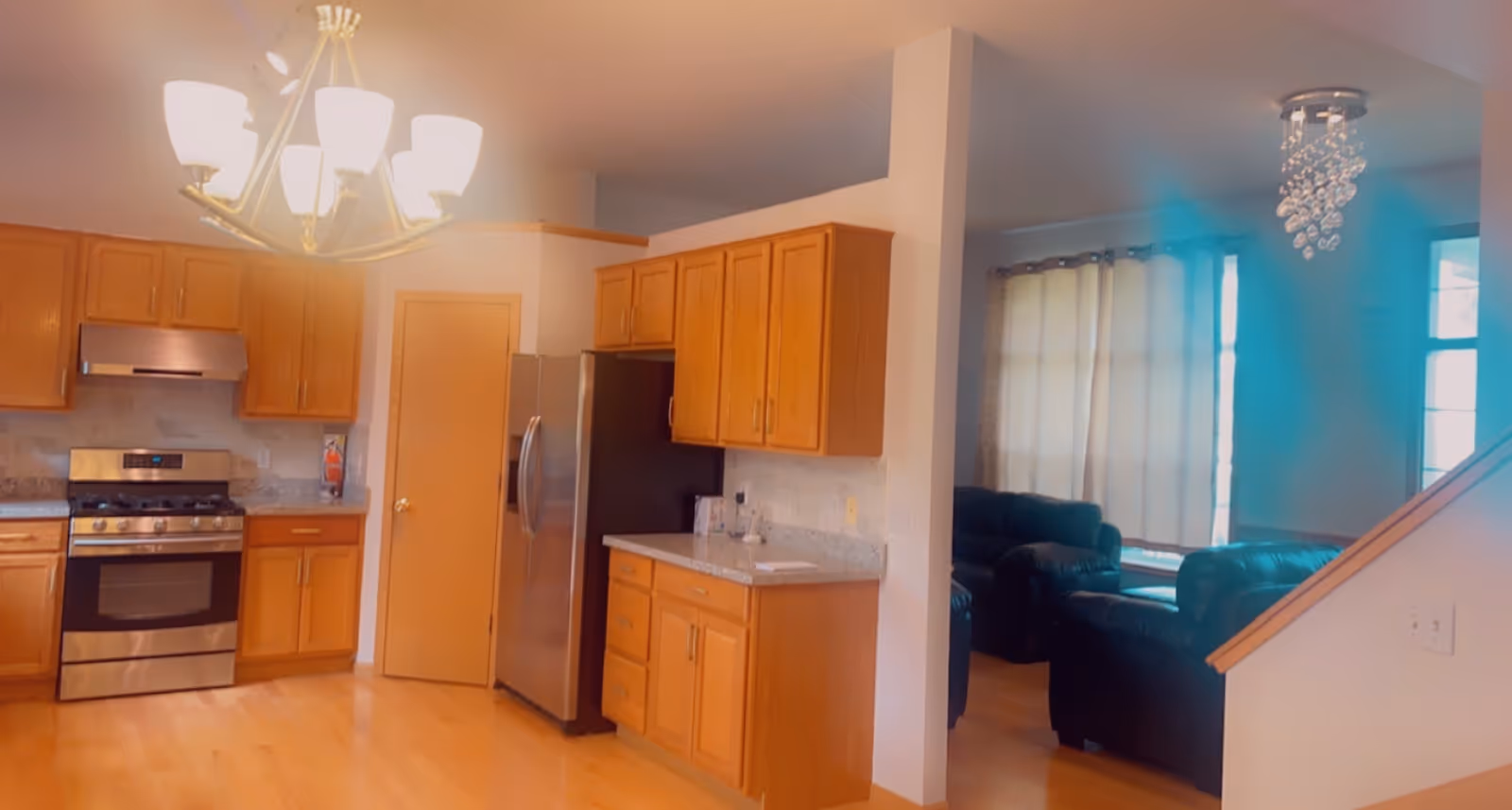 Bright kitchen with wooden cabinets, stainless appliances, and a glimpse of living room seating.