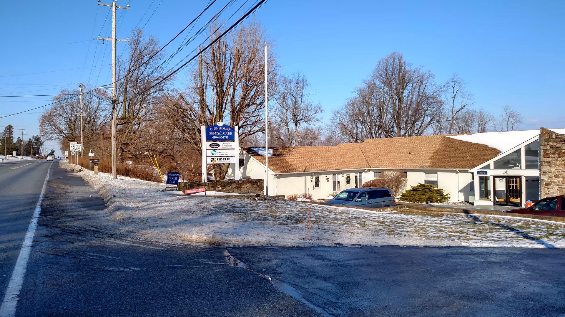 Exterior view of a single-story facility along a road with snow and parked car