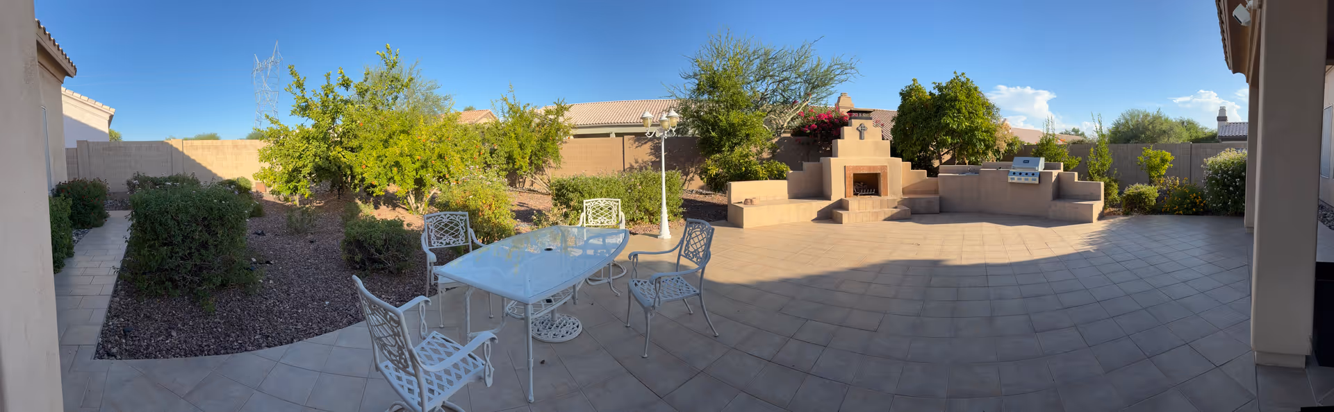 Panoramic view of a tiled outdoor courtyard with a glass table and metal chairs.