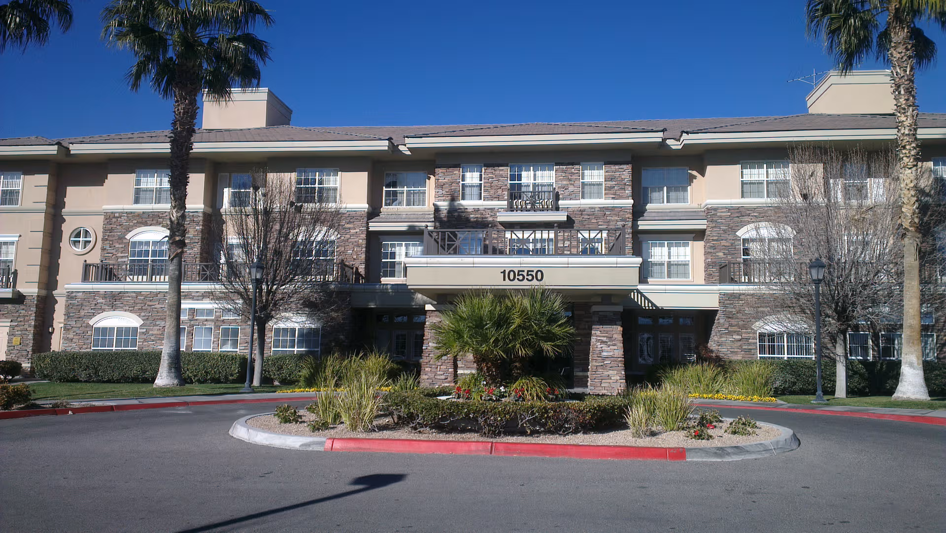Exterior view of The Heights of Summerlin senior living facility, with palm trees and circular driveway.