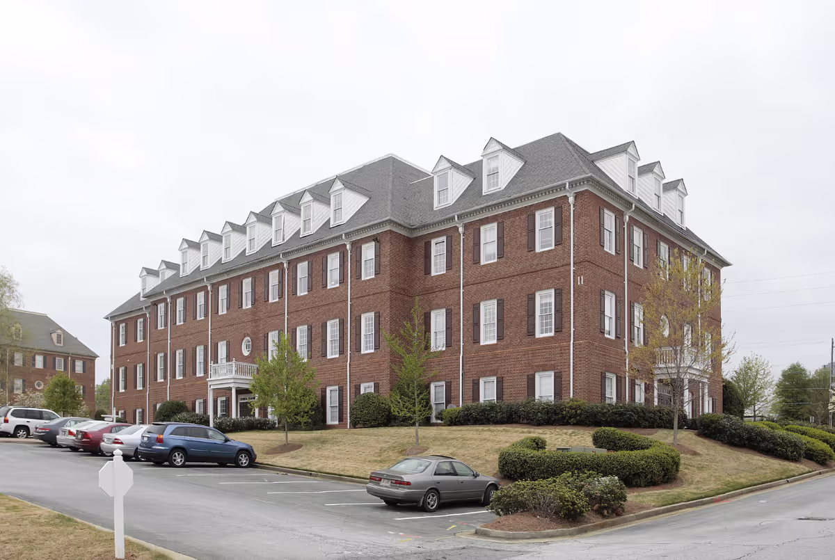 Brick multi-story senior living building with parking lot and manicured lawn.