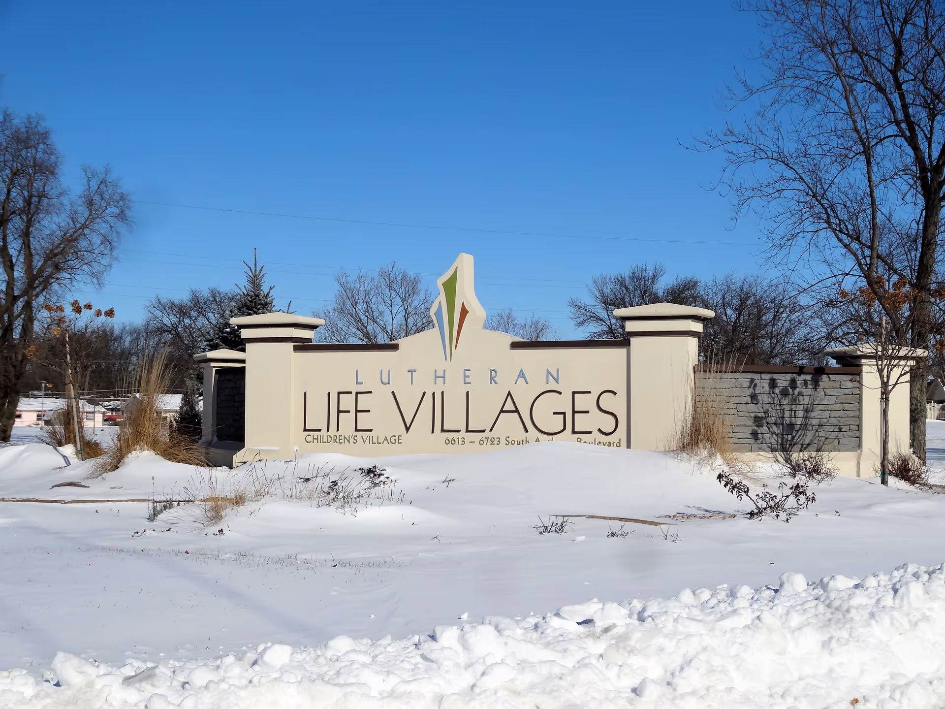 Snowy lawn surrounds the Lutheran Life Villages entrance sign under a clear blue sky.