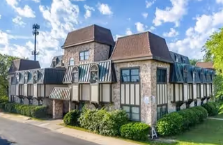 Exterior view of a Tudor-style senior living facility with arched windows and striped awnings.