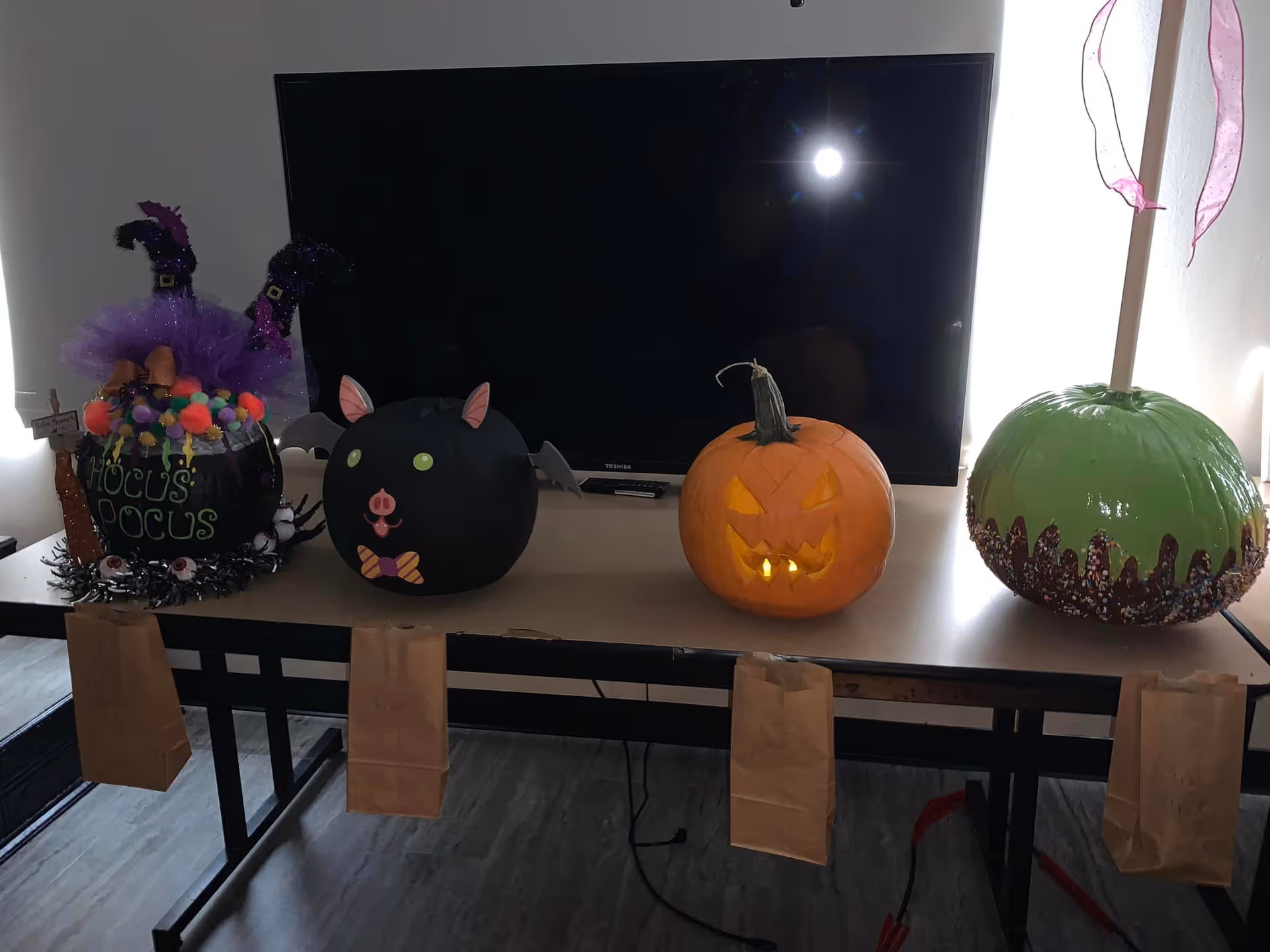 A table in a room displaying four decorated pumpkins and Halloween decorations in front of a large TV.