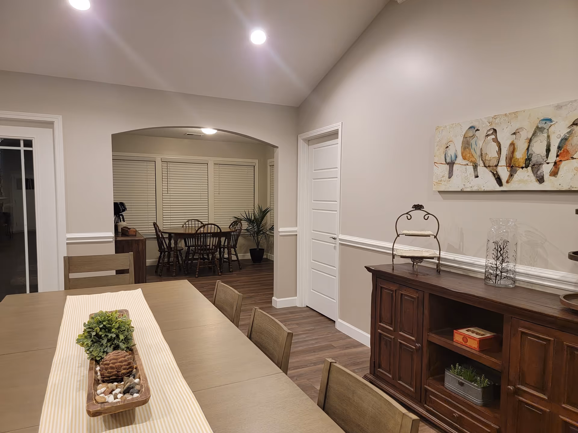 Interior dining area with a long table, chairs, and a sideboard against beige walls.