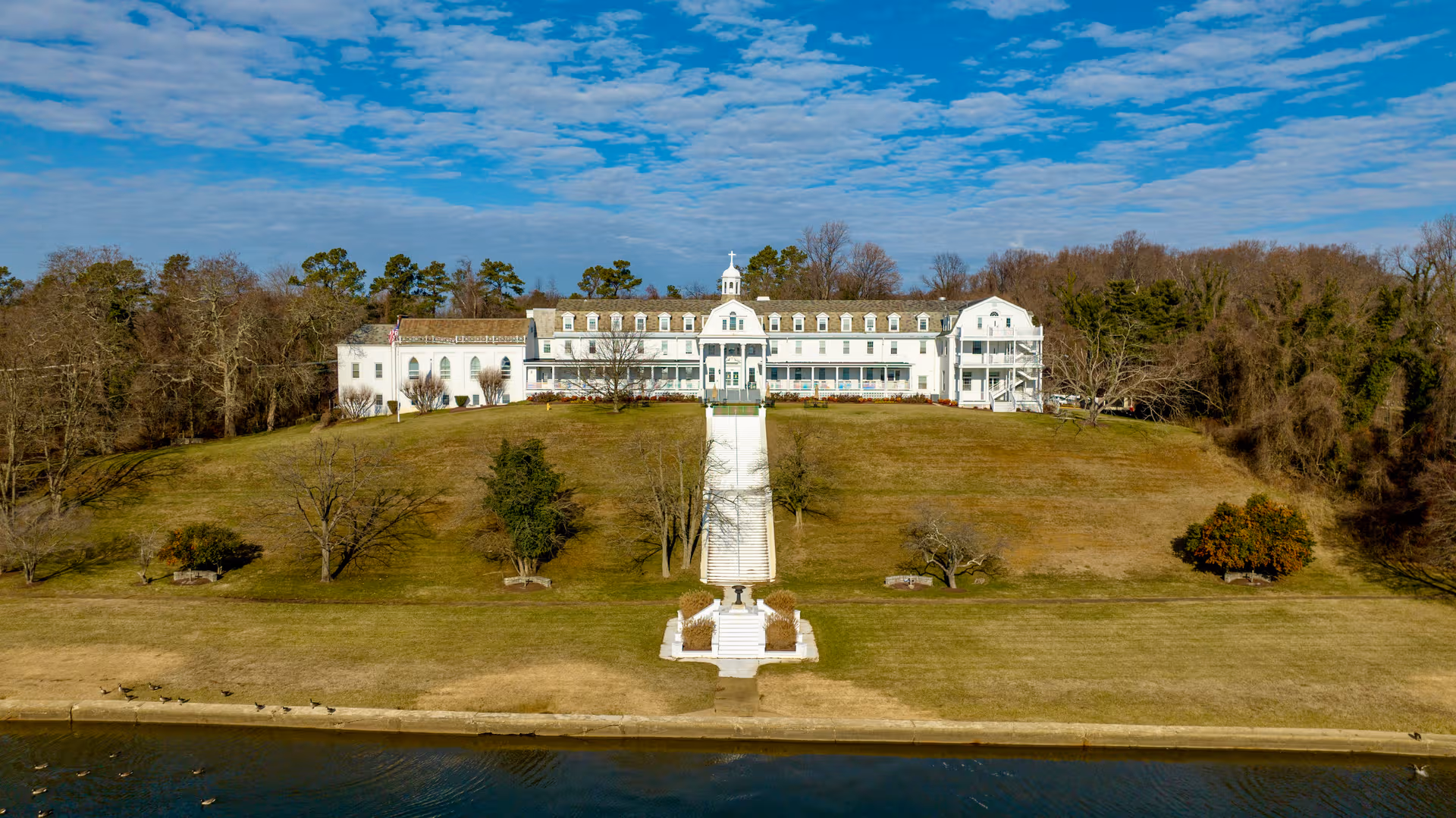 White multi-story senior living building on a hill by the water, with a central staircase.