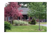Exterior view of a brick nursing home with landscaped front yard and trees.