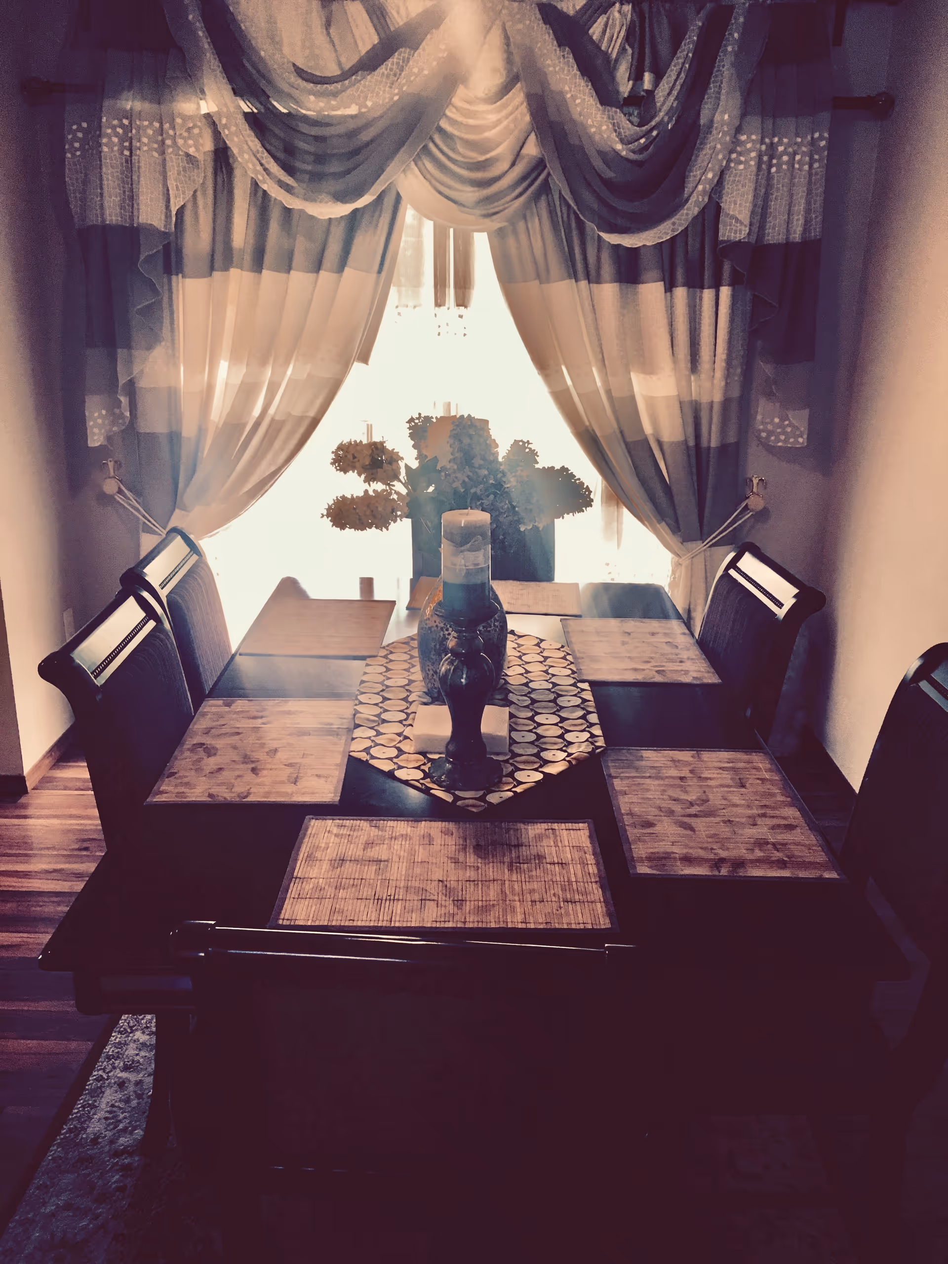 A dining room with a dark table, chairs, window curtains, and a decorative centerpiece.