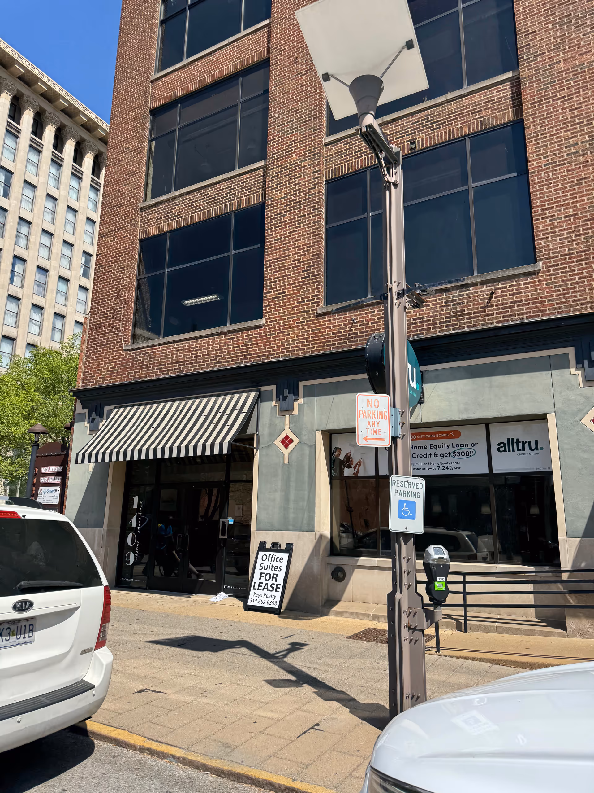 Urban brick building with large glass windows, awning, and street signs along the sidewalk.