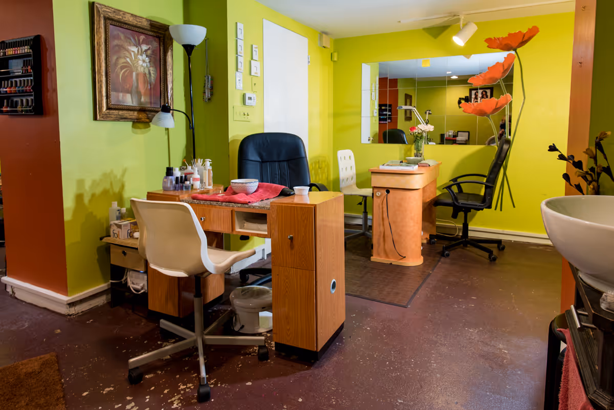 Bright salon inside a senior living facility with chairs, a desk, and a large mirror.