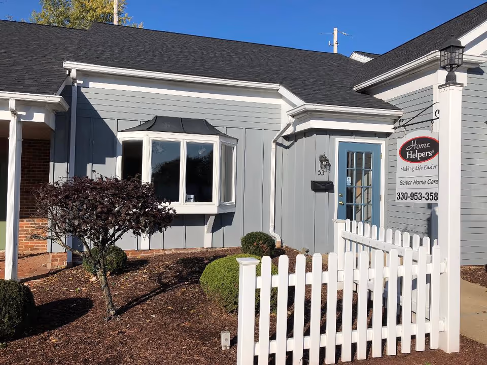Exterior view of a Home Helpers senior care building with a white picket fence.