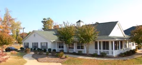Single-story senior living facility with white exterior, front porch, and landscaped entrance.