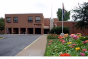 Brick Presbyterian Manors III building exterior with parking, flower beds, and a flagpole.