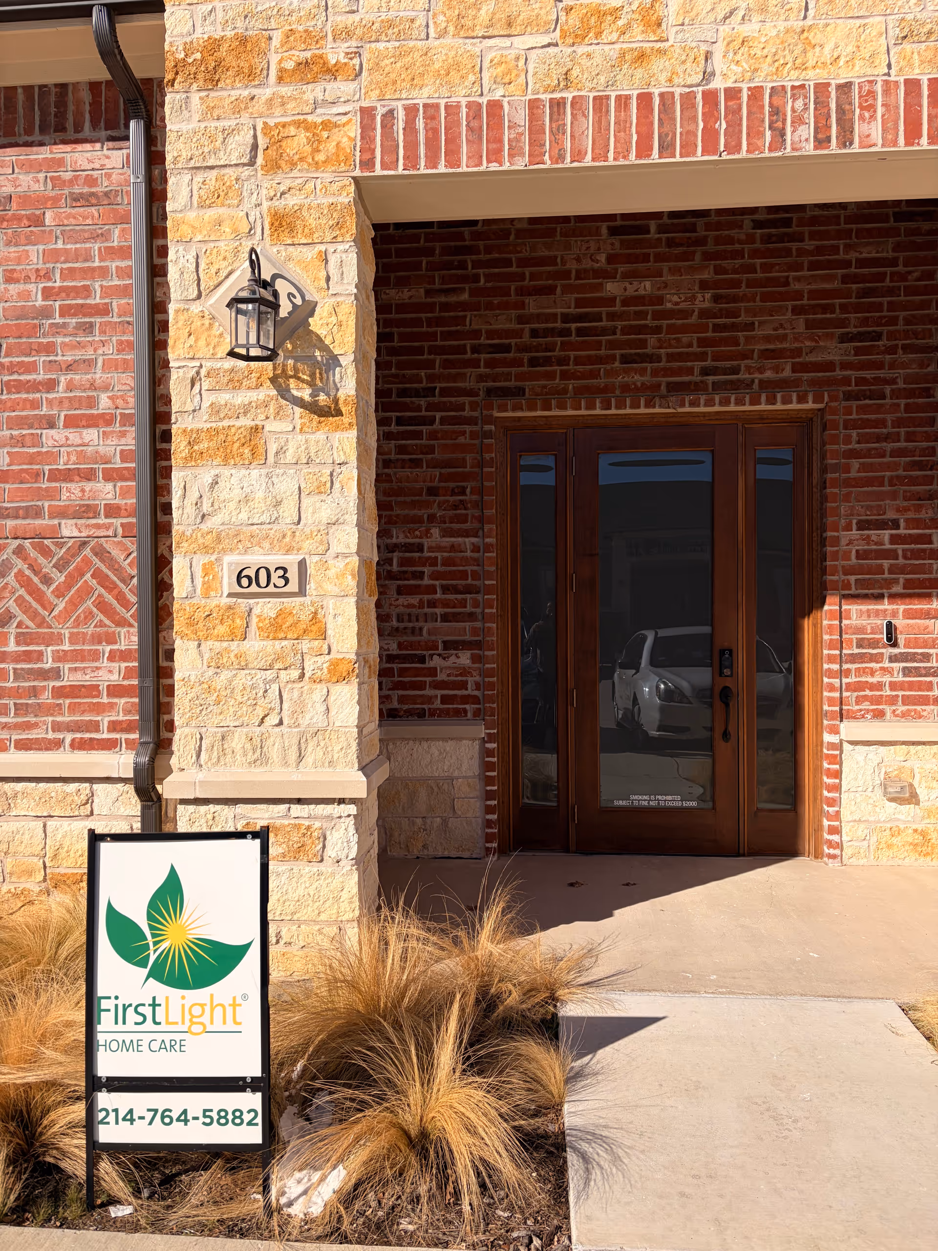 Brick exterior of facility entrance with FirstLight Home Care sign and glass doors.