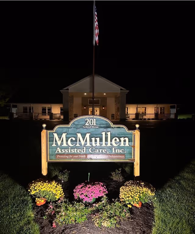 Nighttime view of McMullen Assisted Care sign with colorful flowers and the front of the building.
