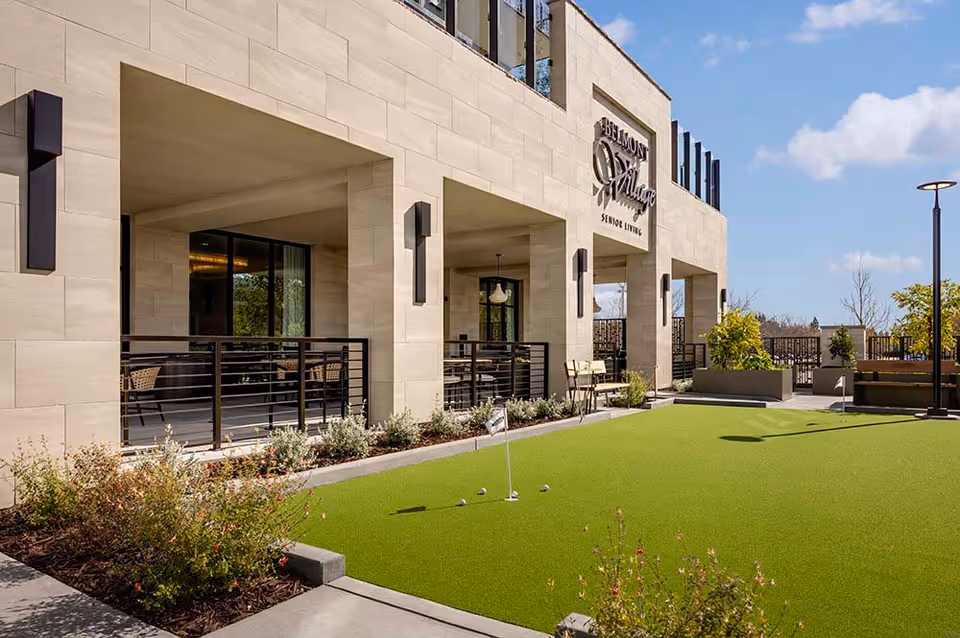 Exterior view of the Belmont Village Senior Living building with a putting green and covered patio seating area.
