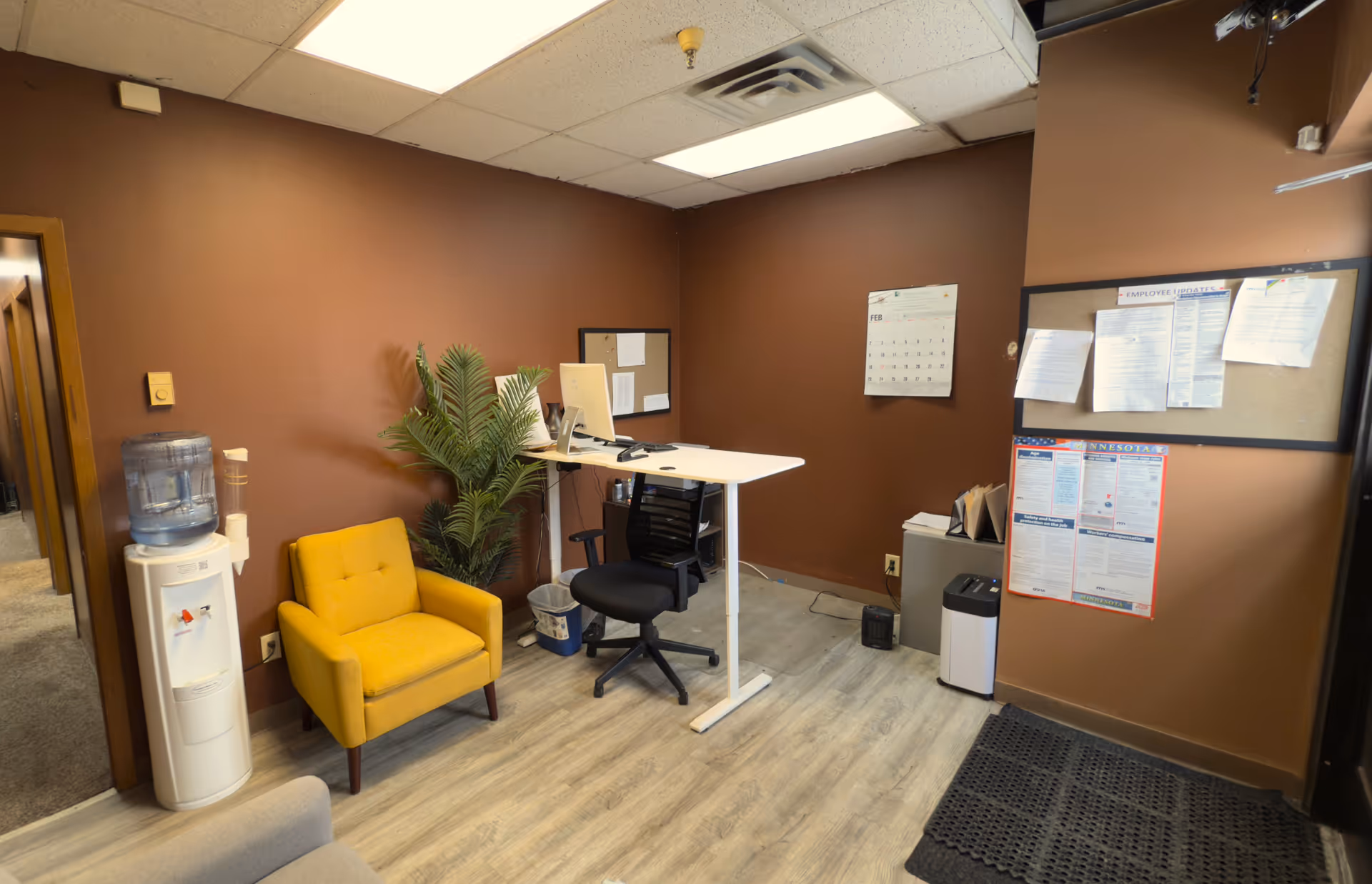 Office reception area with a desk, yellow chair, water cooler, and bulletin boards.