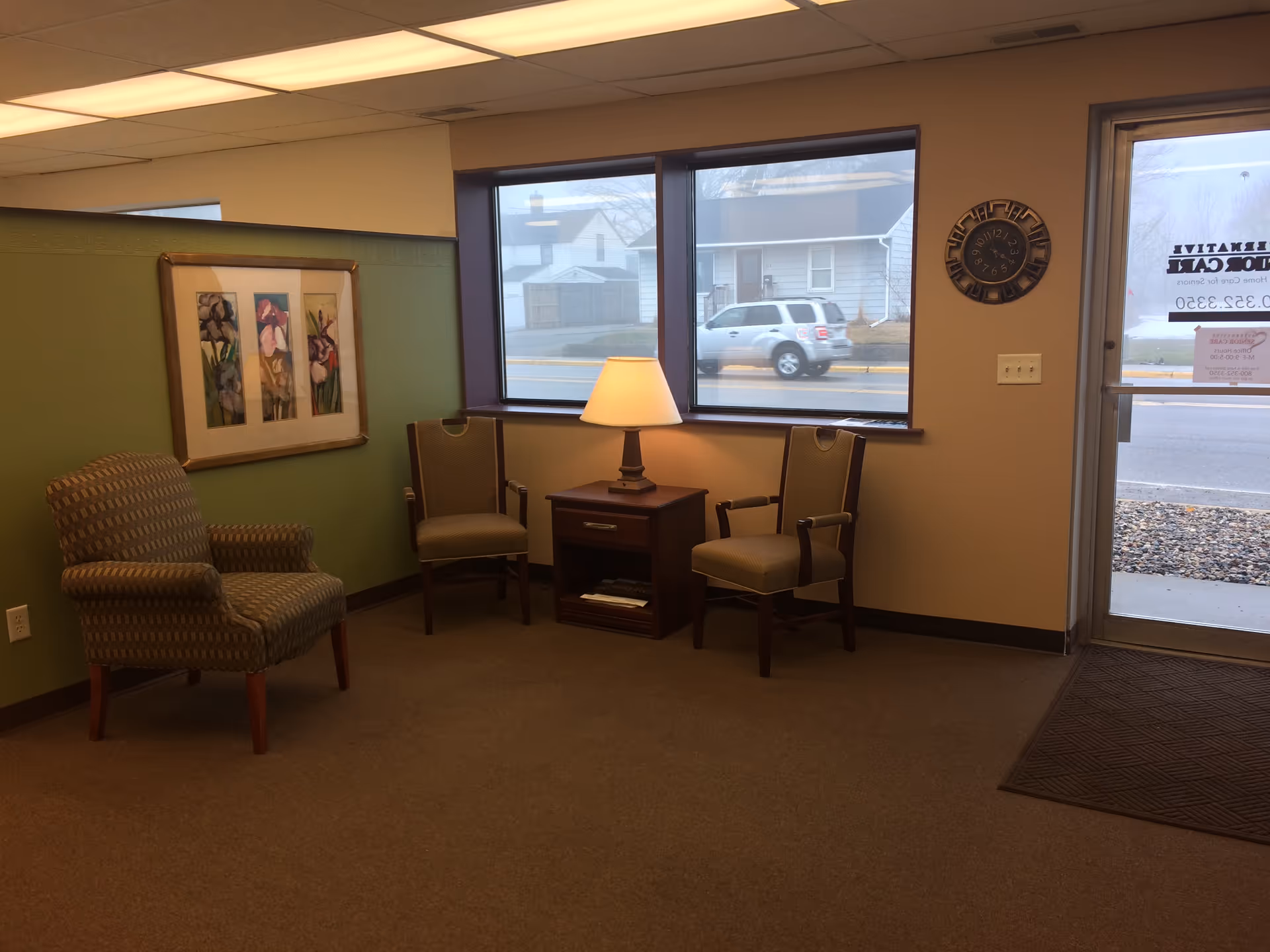 Cozy lounge seating area in a senior facility with chairs, a lamp, and framed art.