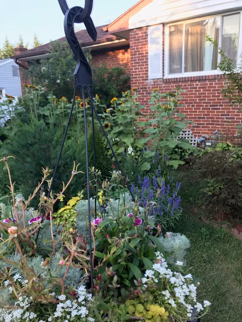 Front yard garden with colorful flowers and a hanging metal plant stand near a brick house