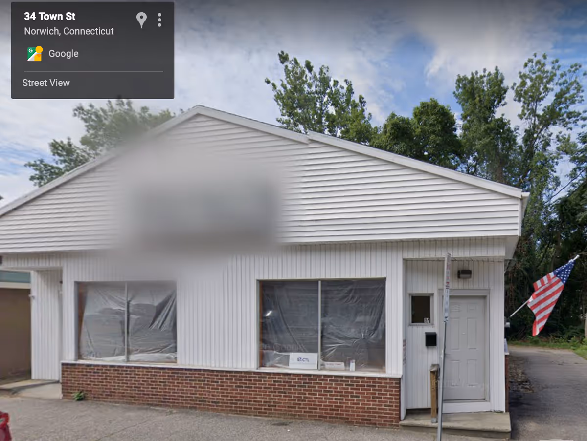 White single-story building with plastic-covered windows and an American flag outside.
