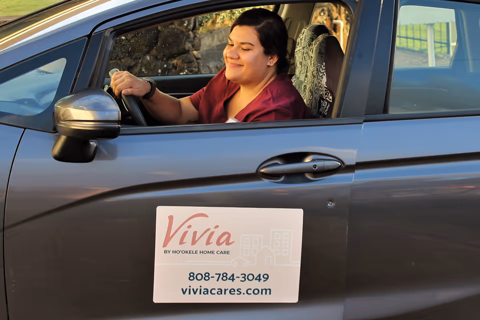 Smiling caregiver drives a branded car for Vivia Cares by Ho'okele Home Care.