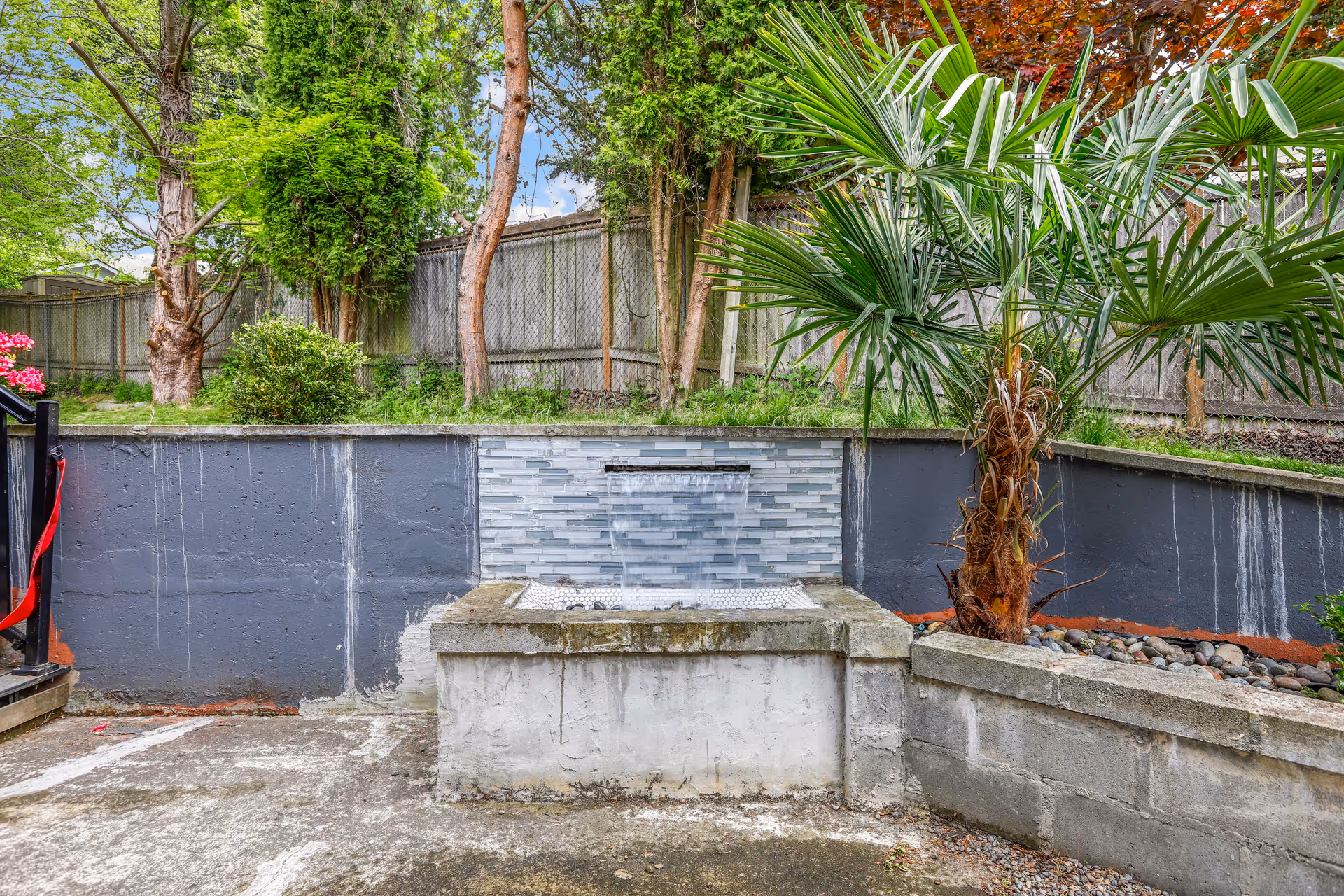 Outdoor courtyard with a small tiled water feature, palm tree, and surrounding greenery.