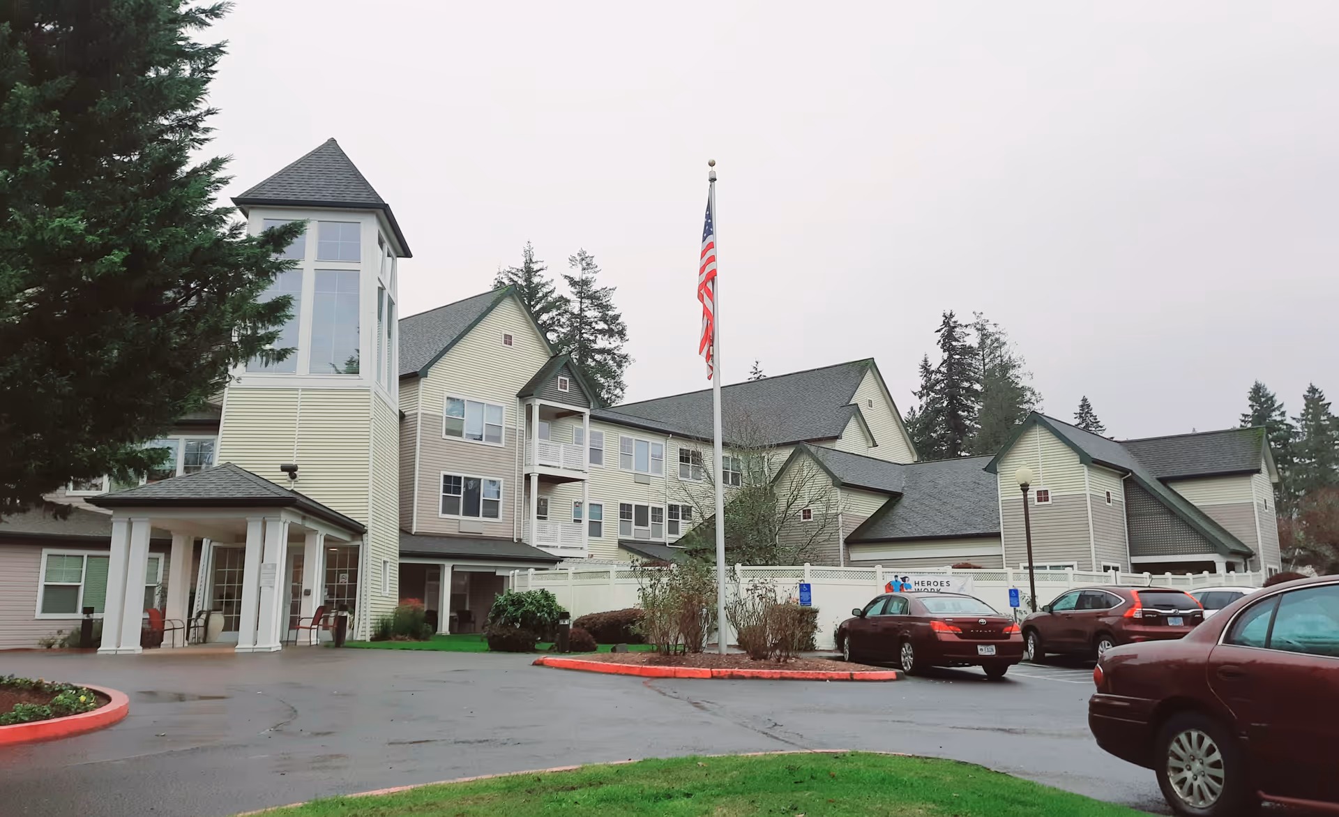 Exterior view of Avamere at Hillsboro, a senior living building with a flagpole and cars.
