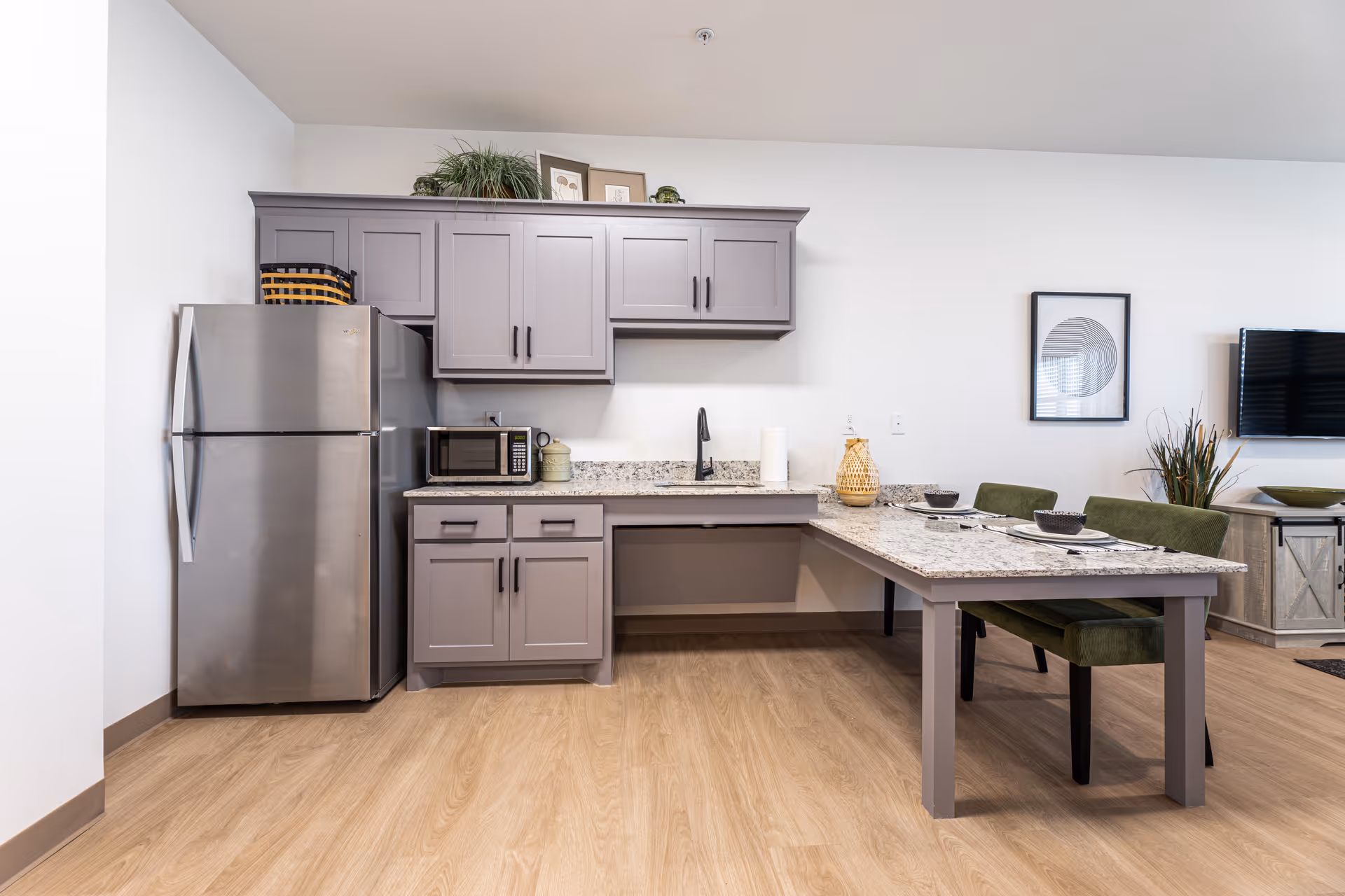 Modern kitchen area with granite countertops, gray cabinets, a dining island, and stainless steel refrigerator.
