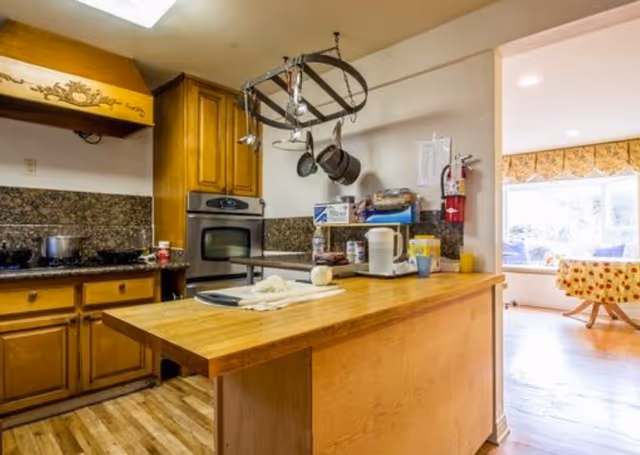 Cozy kitchen with island, hanging pots, and adjacent dining area in a senior living facility.
