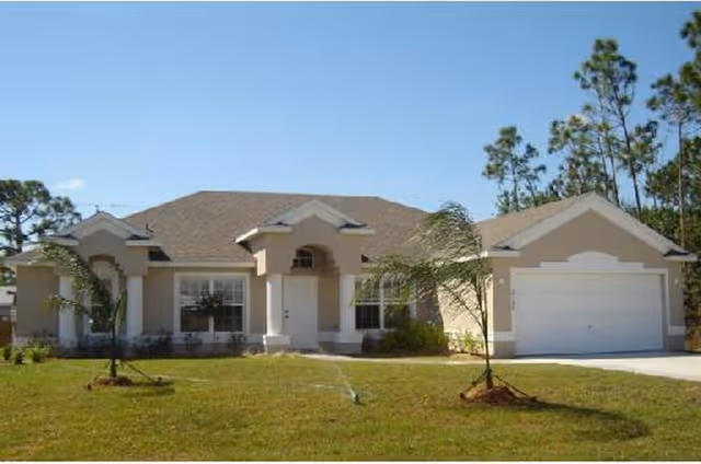 Single-story beige house with front entrance, two-car garage, and manicured lawn.