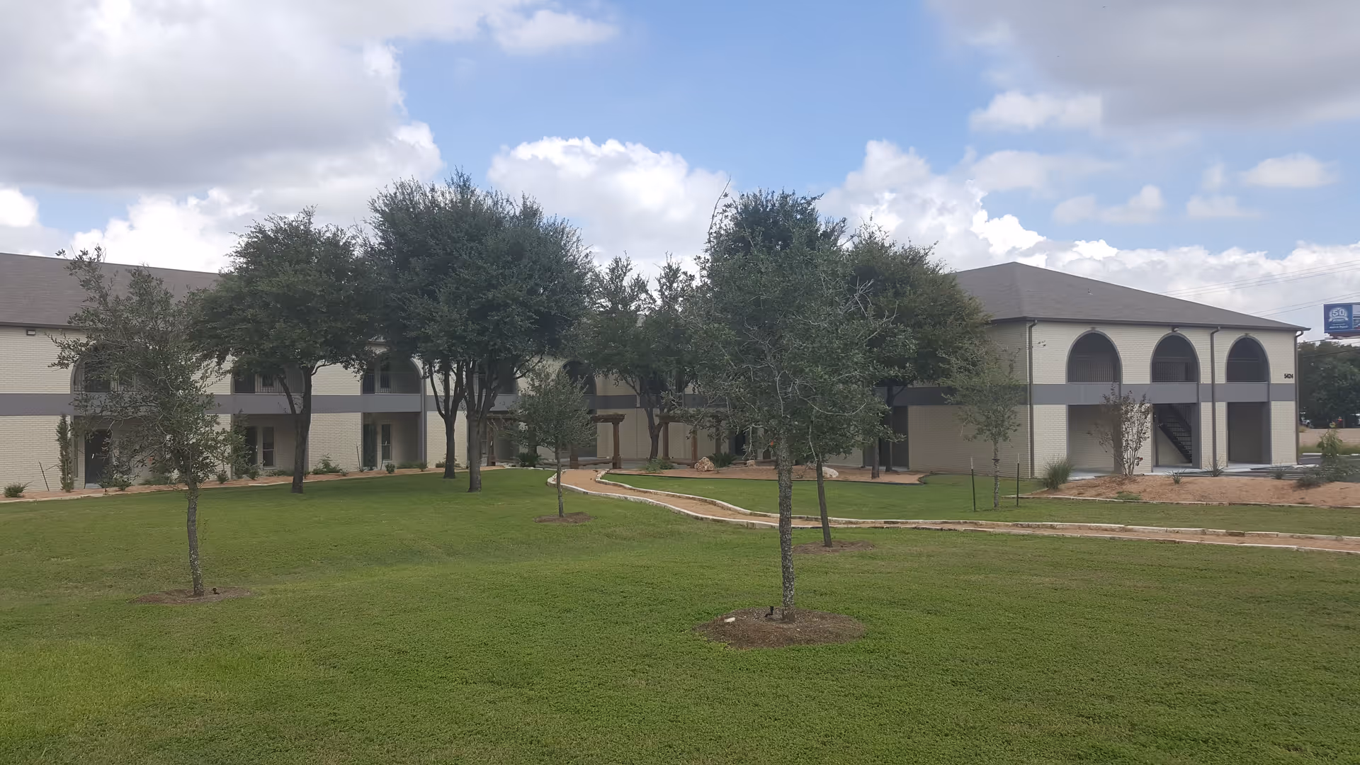 Exterior view of a Comfort Keepers facility with arches, trees, and a green lawn.