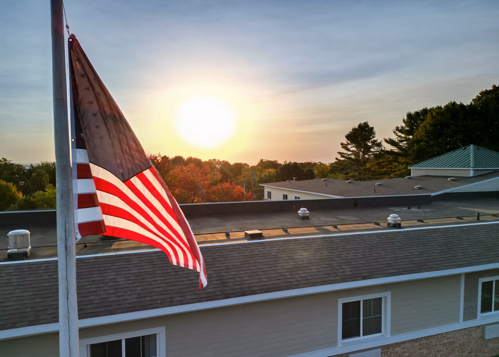 American flag on a flagpole beside the rooftop of a senior living building at sunset.