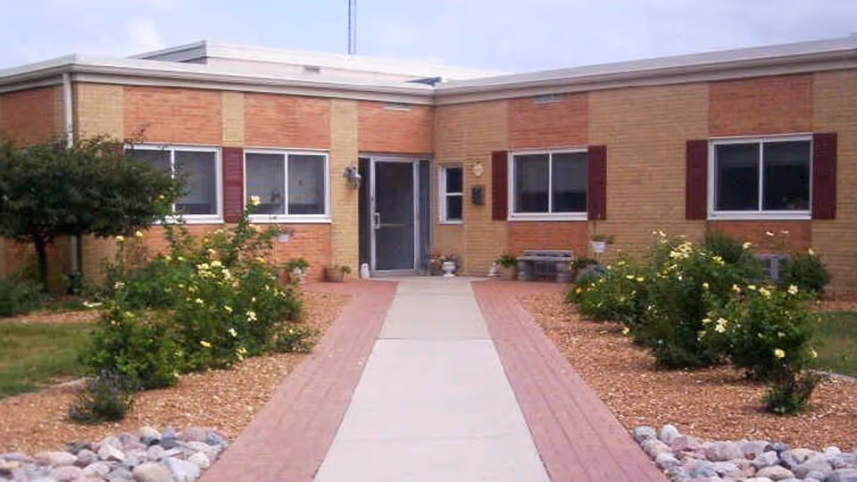 Brick single-story nursing facility exterior with a central walkway and landscaped beds.