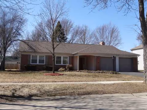 Suburban single-story brick house with attached two-car garage and leafless trees.