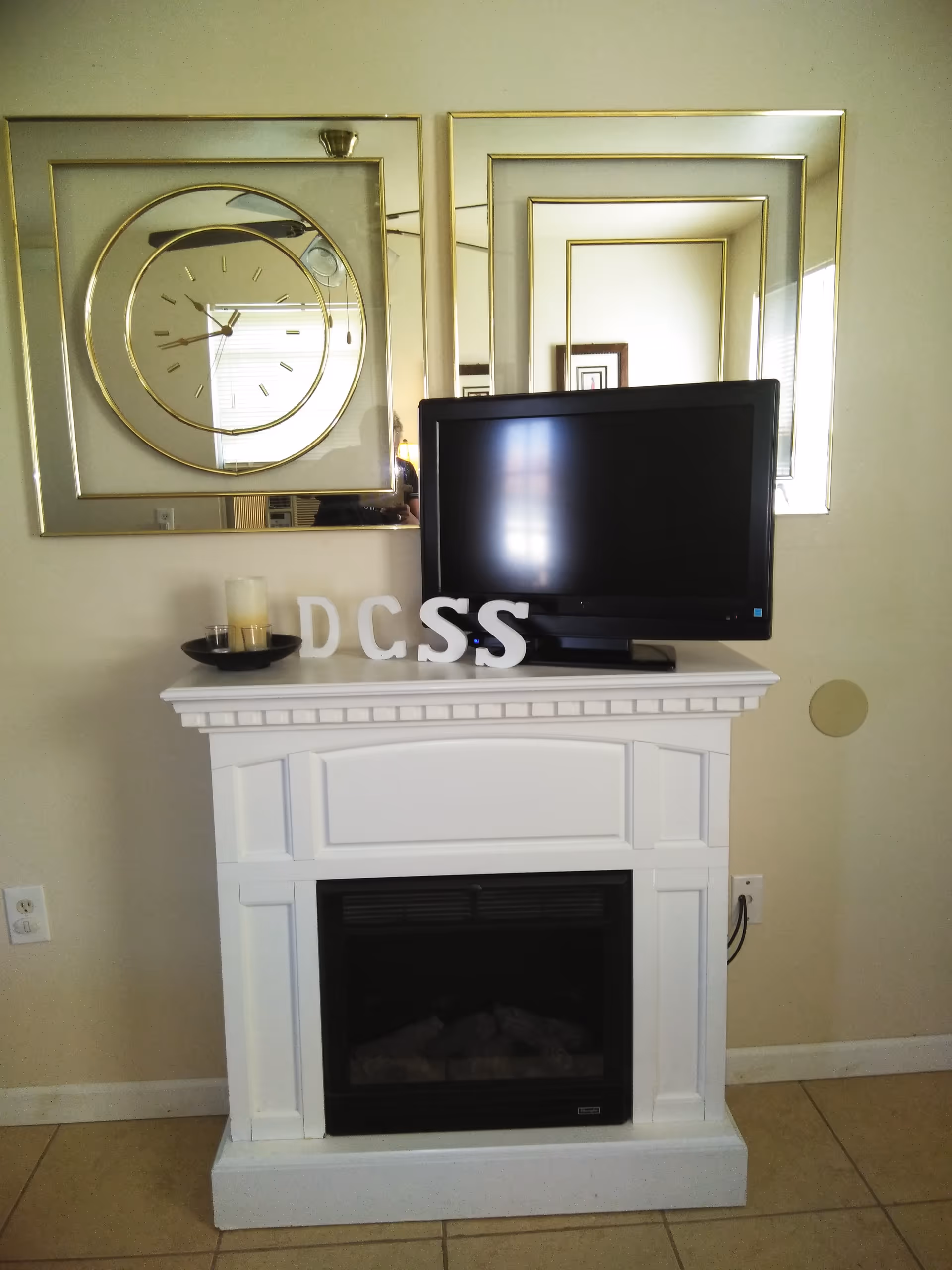 White fireplace mantel with a TV and circular mirrored art above.