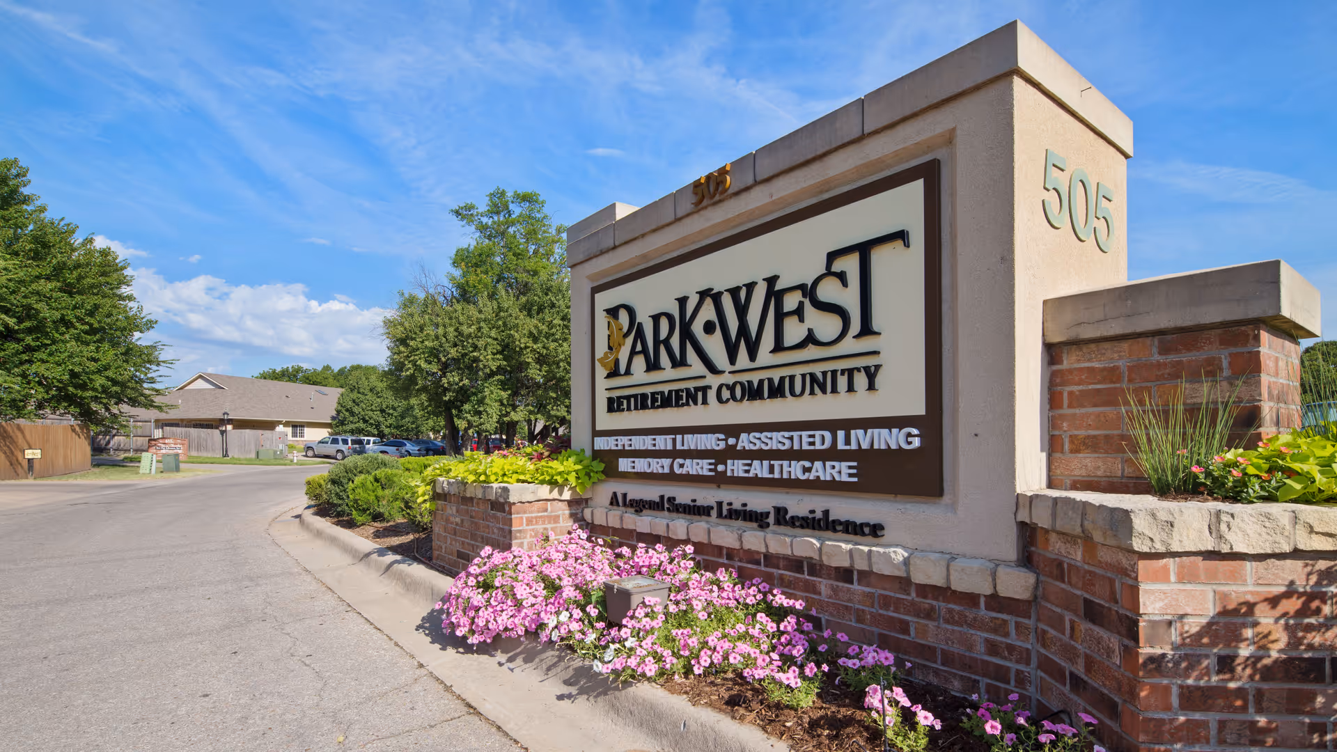 Entrance sign for Park West Retirement Community with landscaped flower bed and clear blue sky