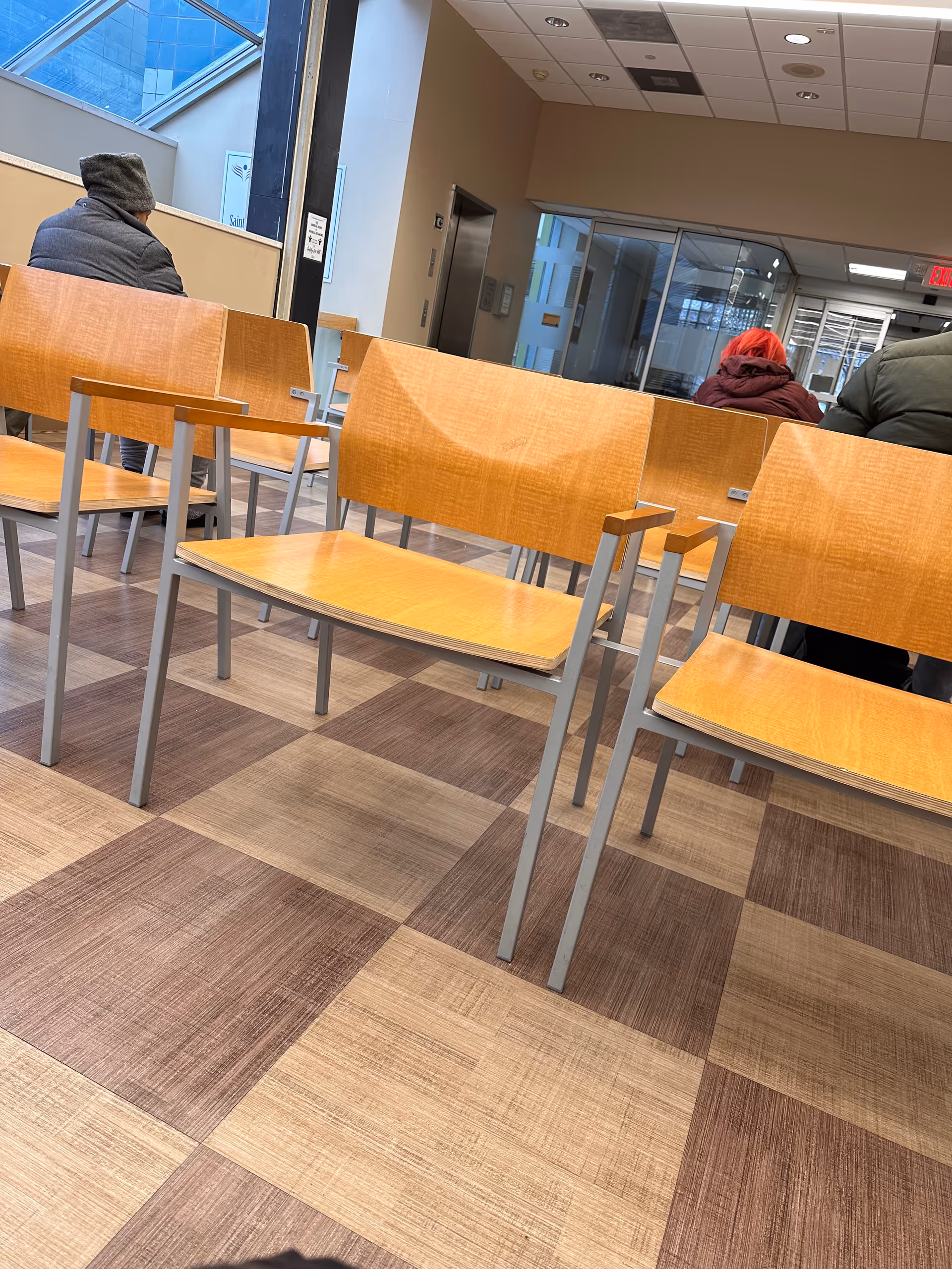 Rows of wooden chairs in a clinic waiting area with people seated.