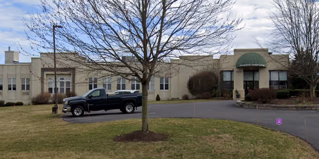 Front exterior of Greenfield Senior Living building with green awning entrance and pickup truck.