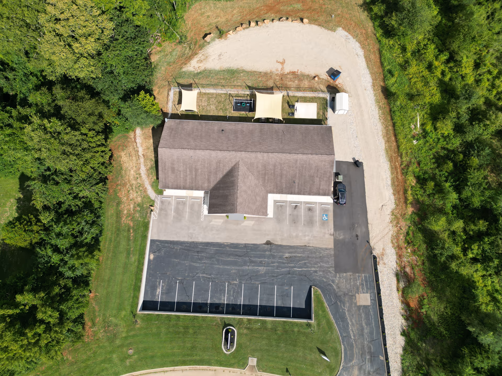 Aerial view of a single-story facility with a parking lot and surrounding trees.