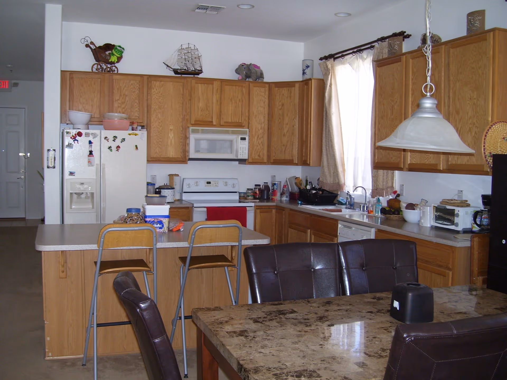 Open kitchen with wooden cabinets, an island with stools, a dining table and chairs, and various appliances on the counters.