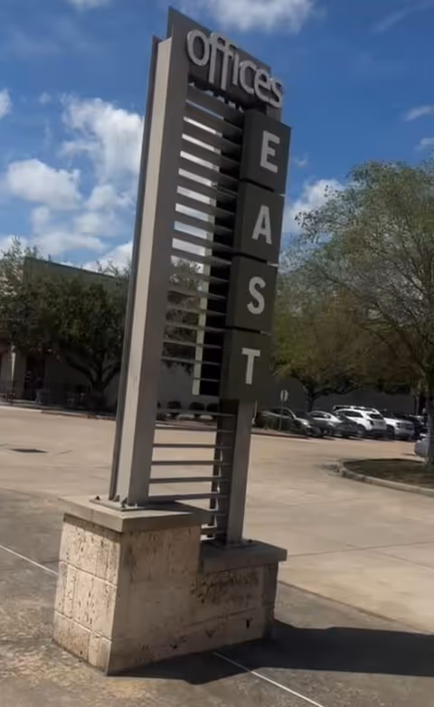 Tall outdoor sign reading 'Offices East' beside a parking lot with trees.