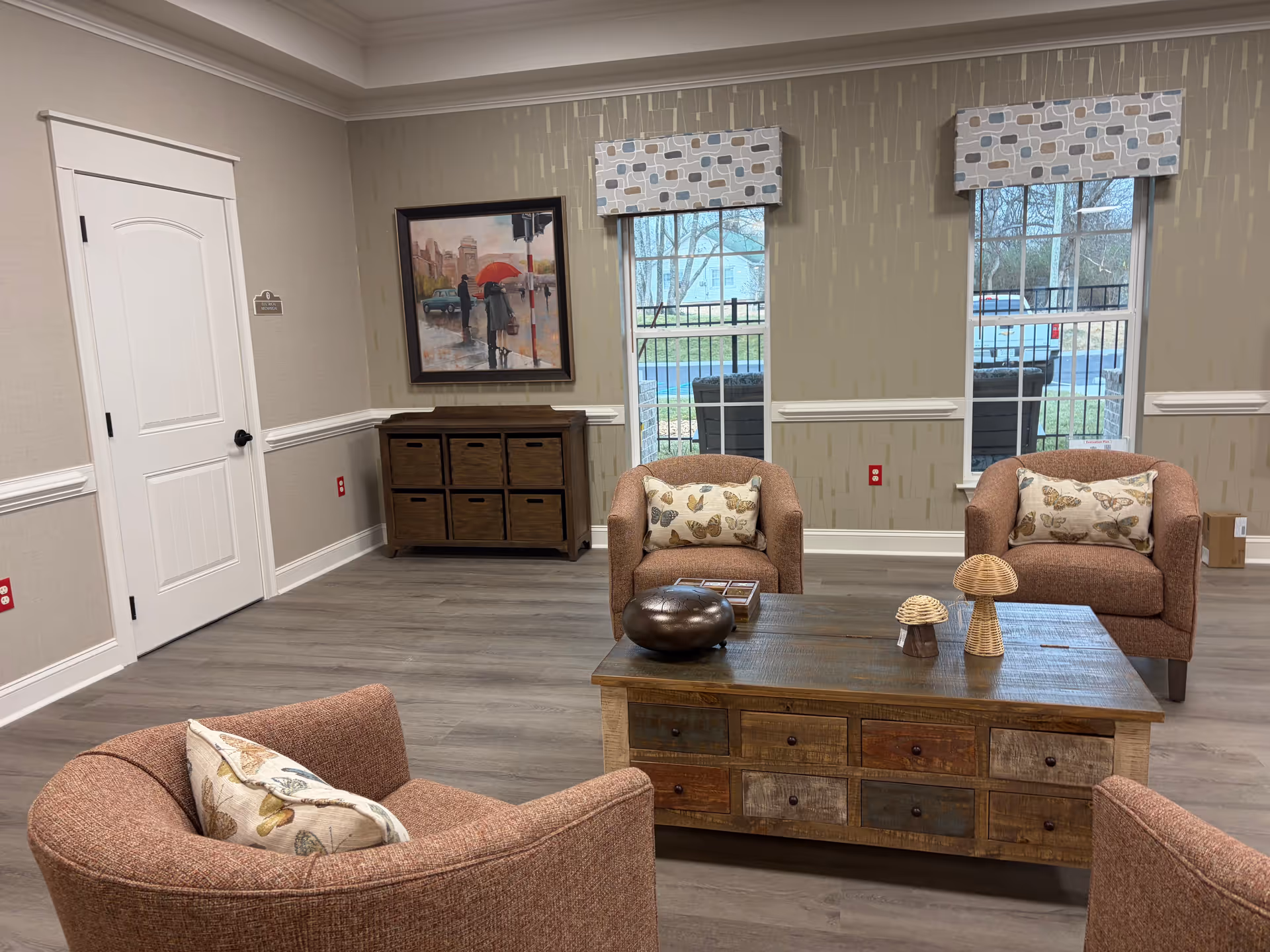 Cozy senior living lounge with brown chairs, wooden coffee table, decorative pillows, and windows.