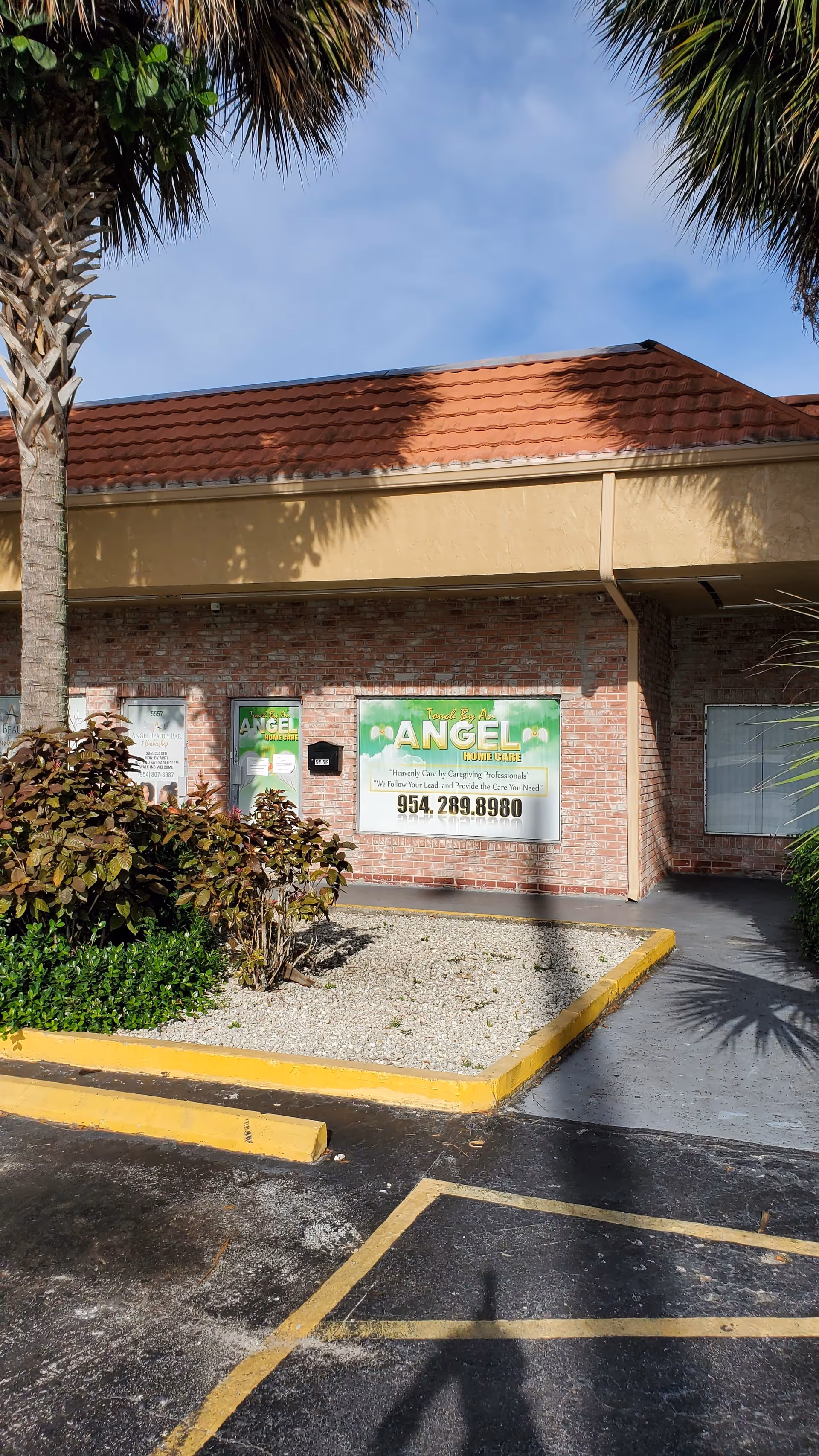 Exterior of a brick facility with palm trees, signage, and a parking lot.