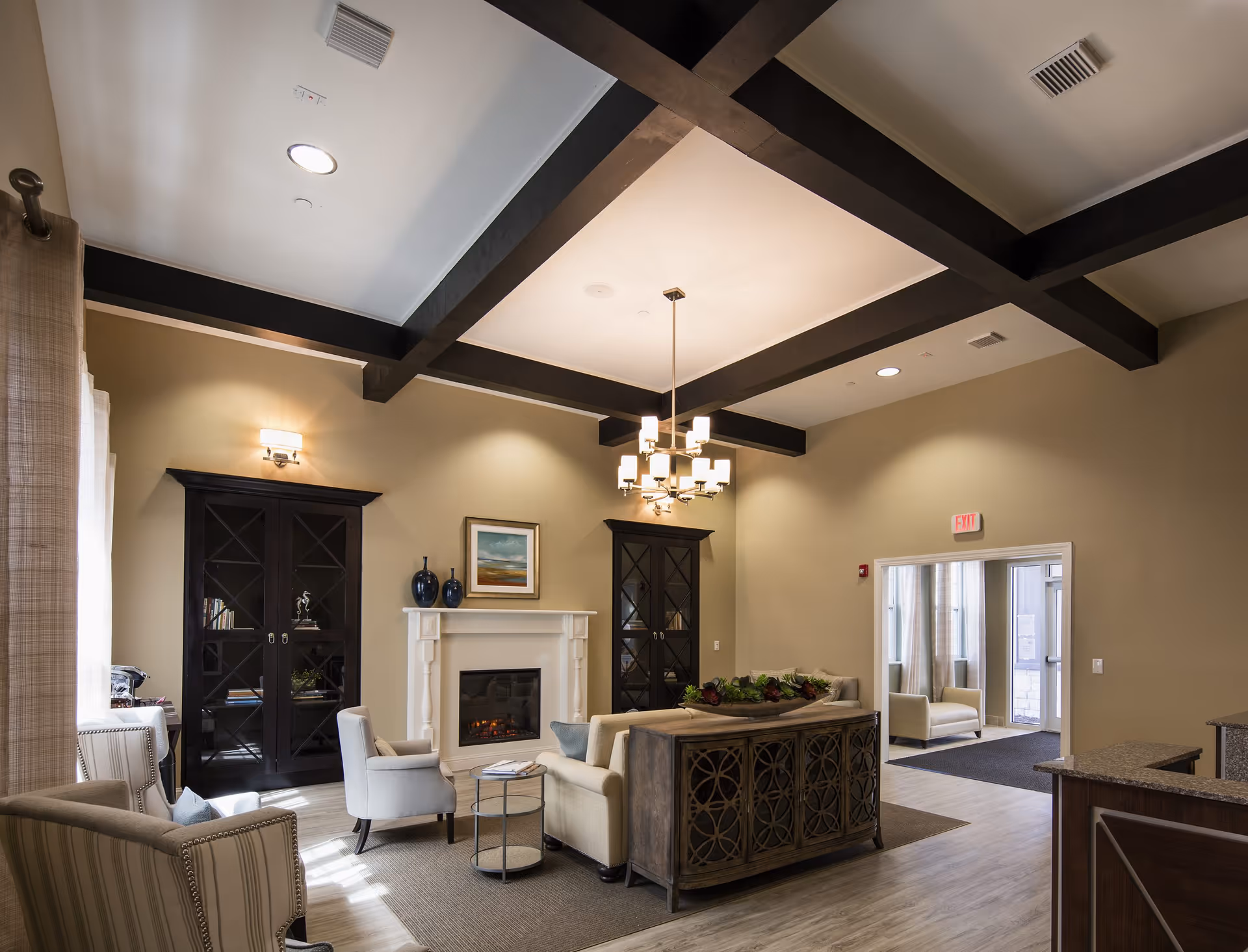 Spacious senior living lounge with fireplace, dark wood beams, and comfortable seating.