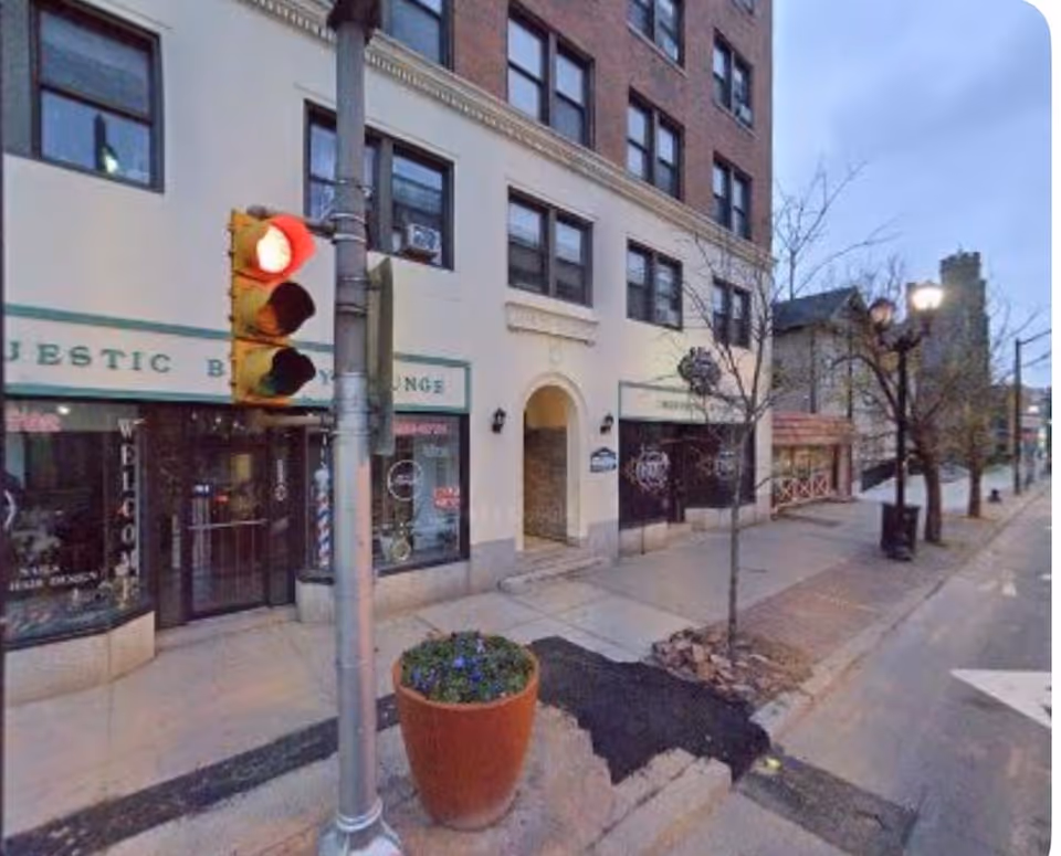 Urban street view of a storefront-lined building with a traffic signal and planter