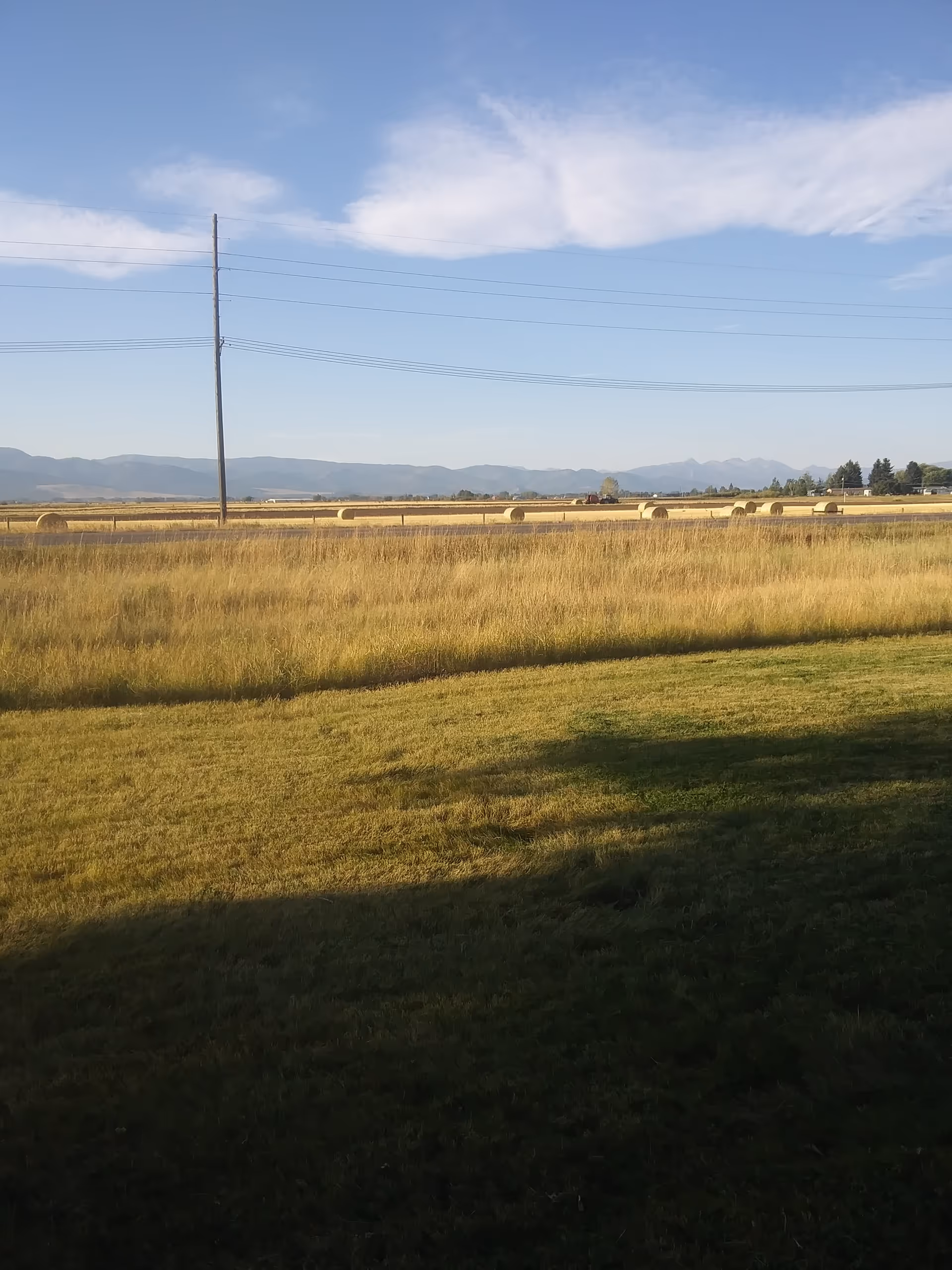 Rural field with hay bales, power lines, and distant mountains under blue sky.