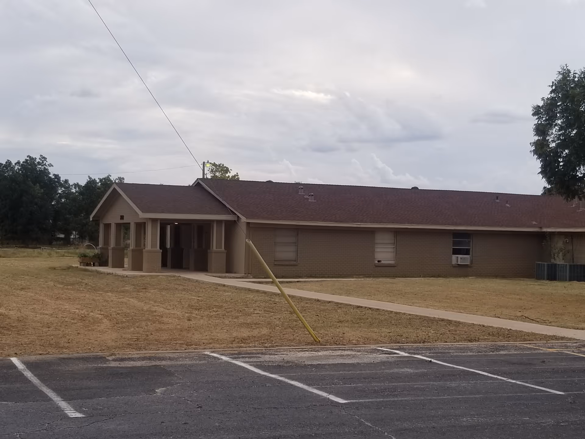 One-story brick building with a covered entrance, dry lawn, and adjacent parking lot.